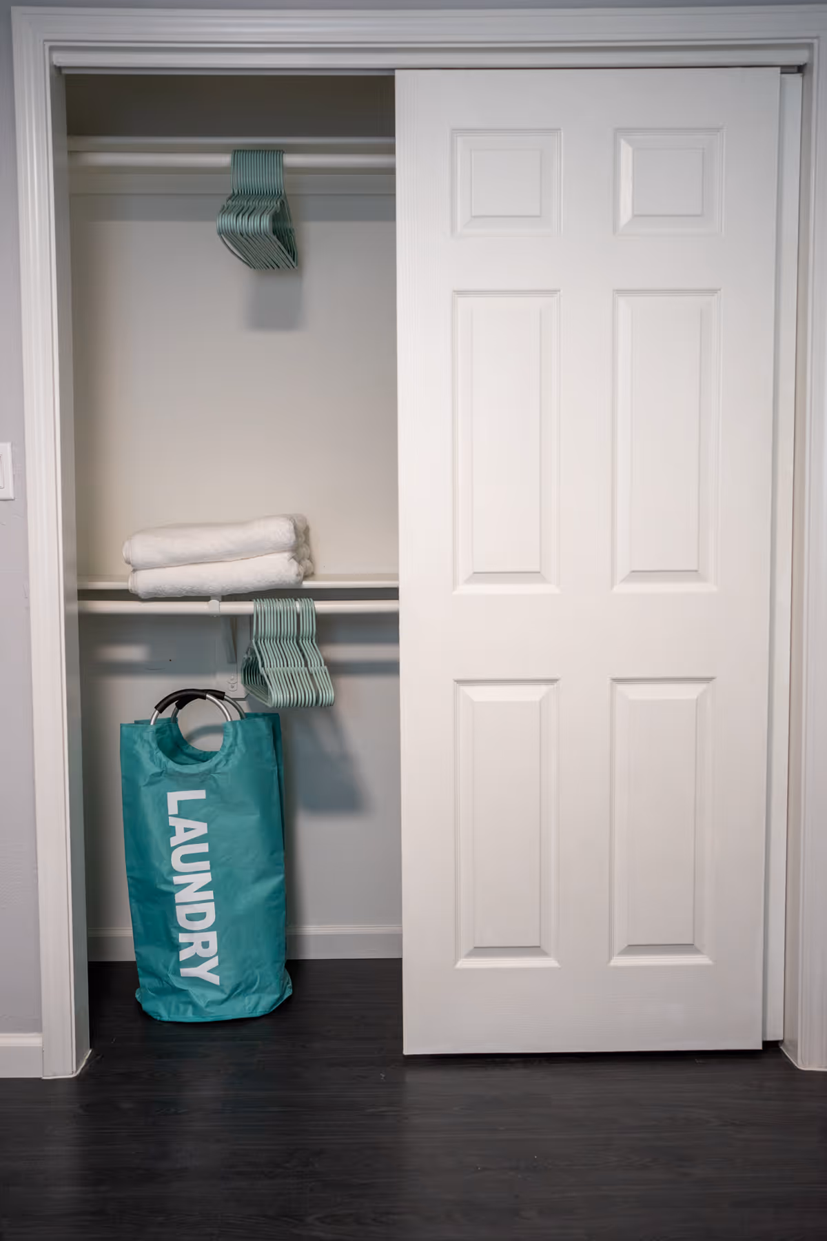 Open closet with hangers, folded towels, and a turquoise laundry bag labeled LAUNDRY
