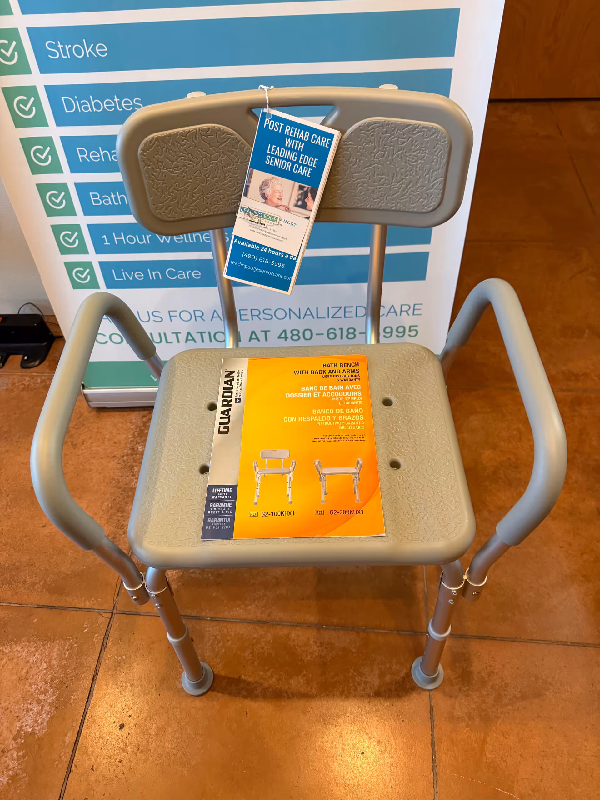 Grey assistive chair with backrest and brochures in front of a blue banner in a lobby.