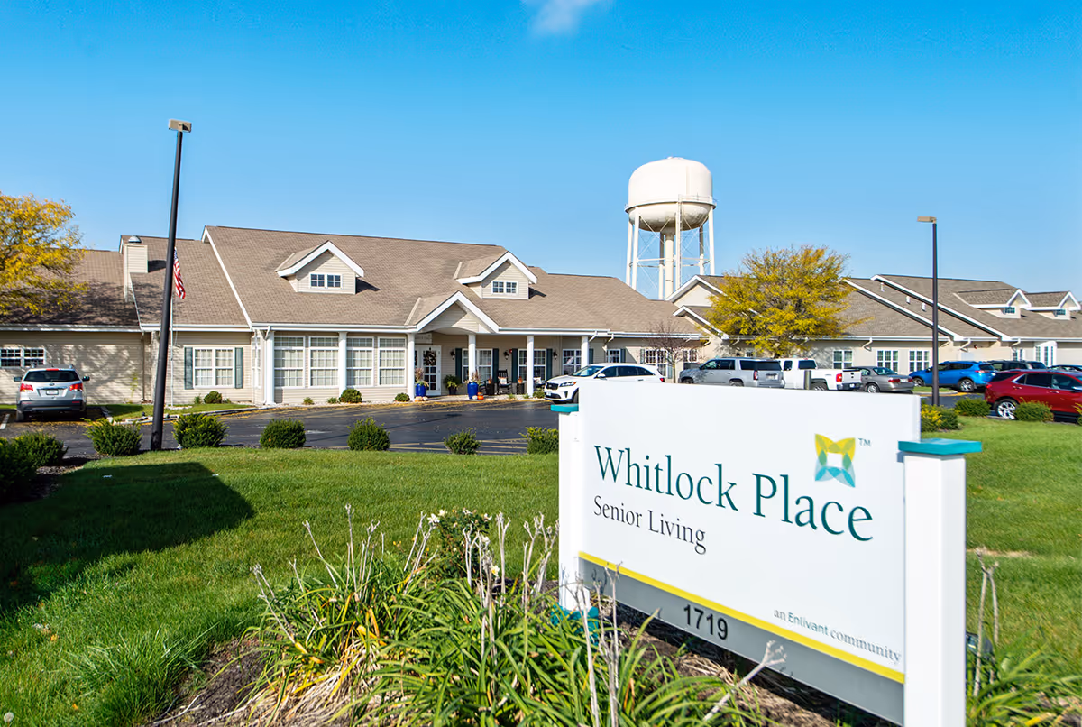 Whitlock Place Senior Living exterior with sign, single-story building, parking lot, and blue sky.