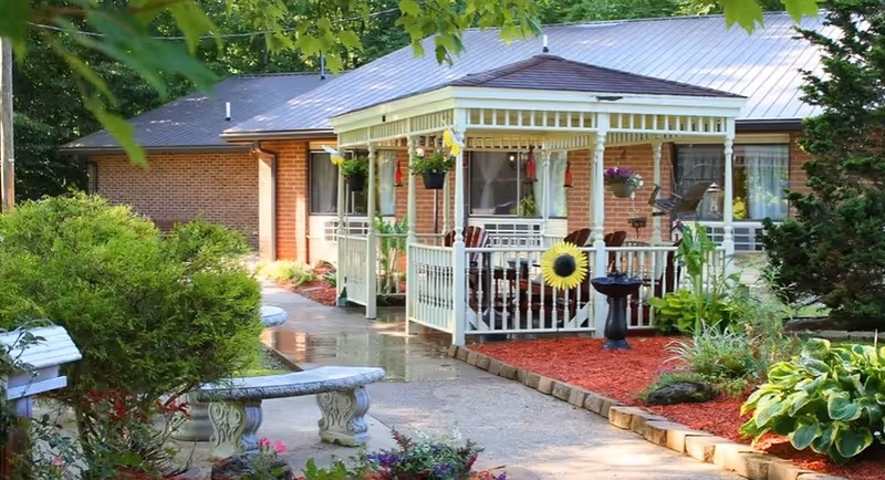 Senior living facility exterior with brick facade and white porch, surrounded by greenery.