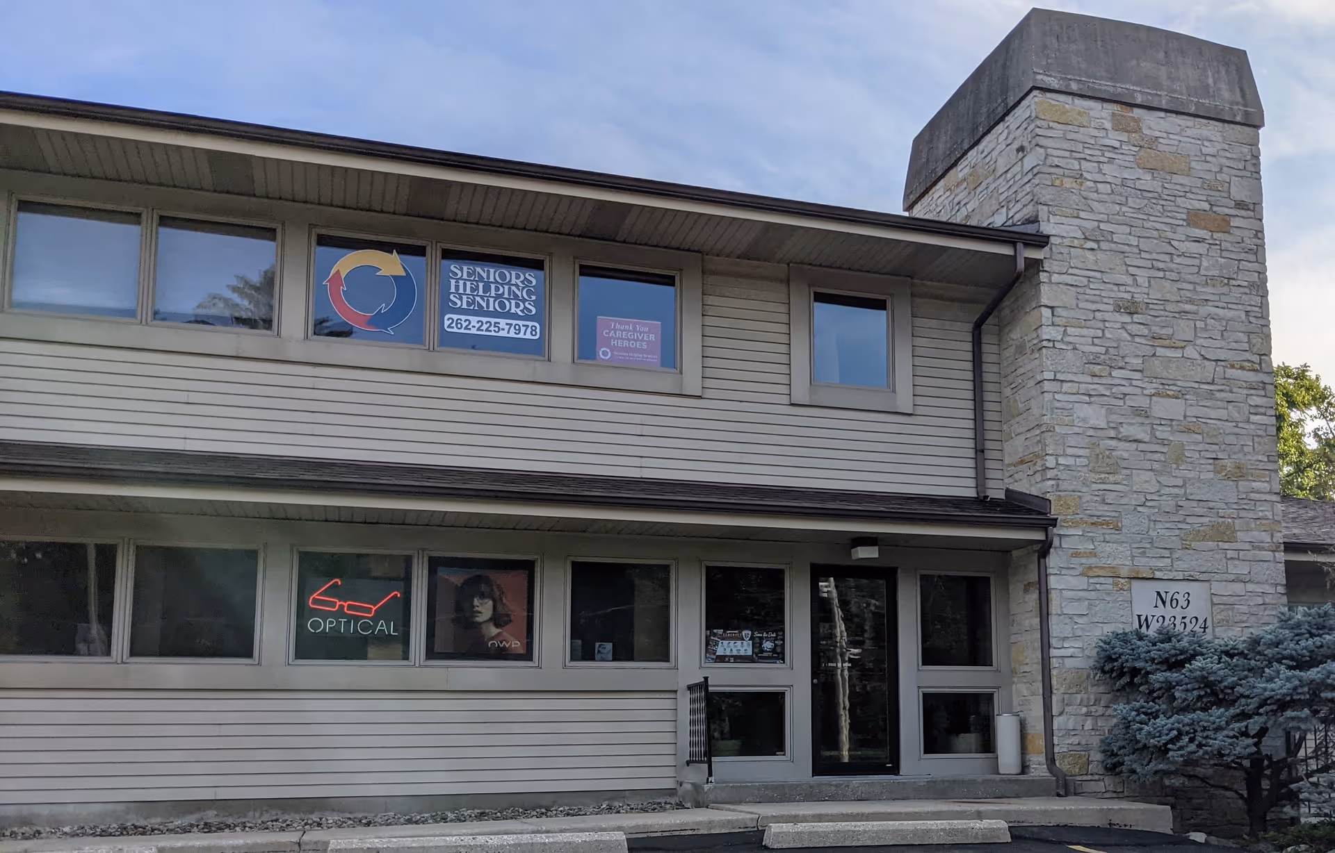 Two-story facility exterior with stone chimney and Seniors Helping Seniors signs on windows.