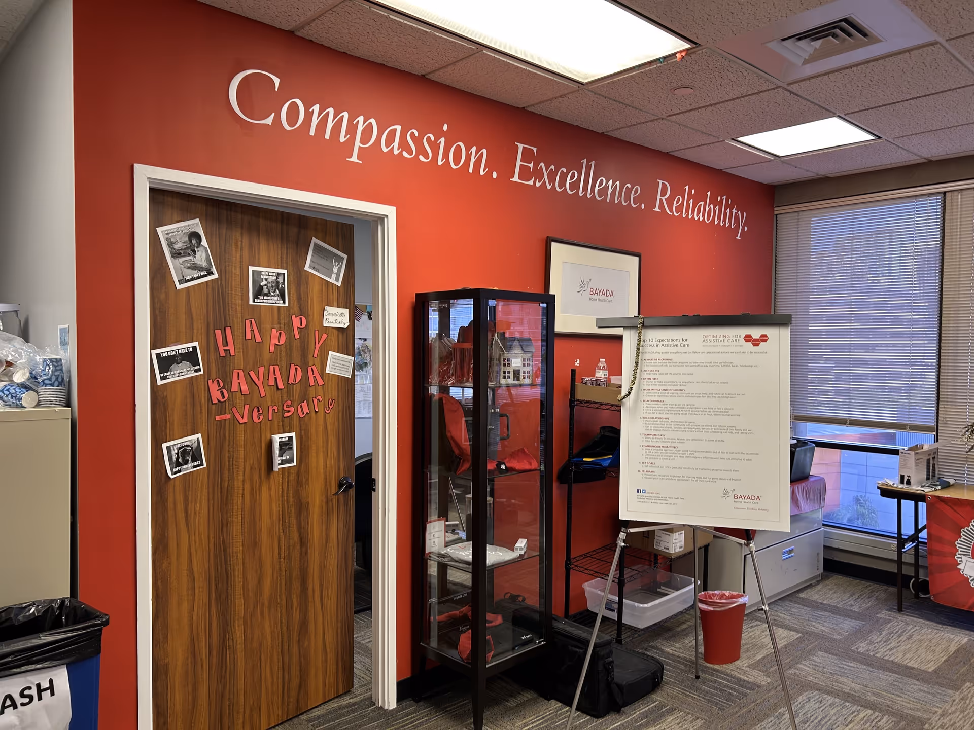 Interior office area with red wall, inspirational phrases, a display cabinet, and a whiteboard.