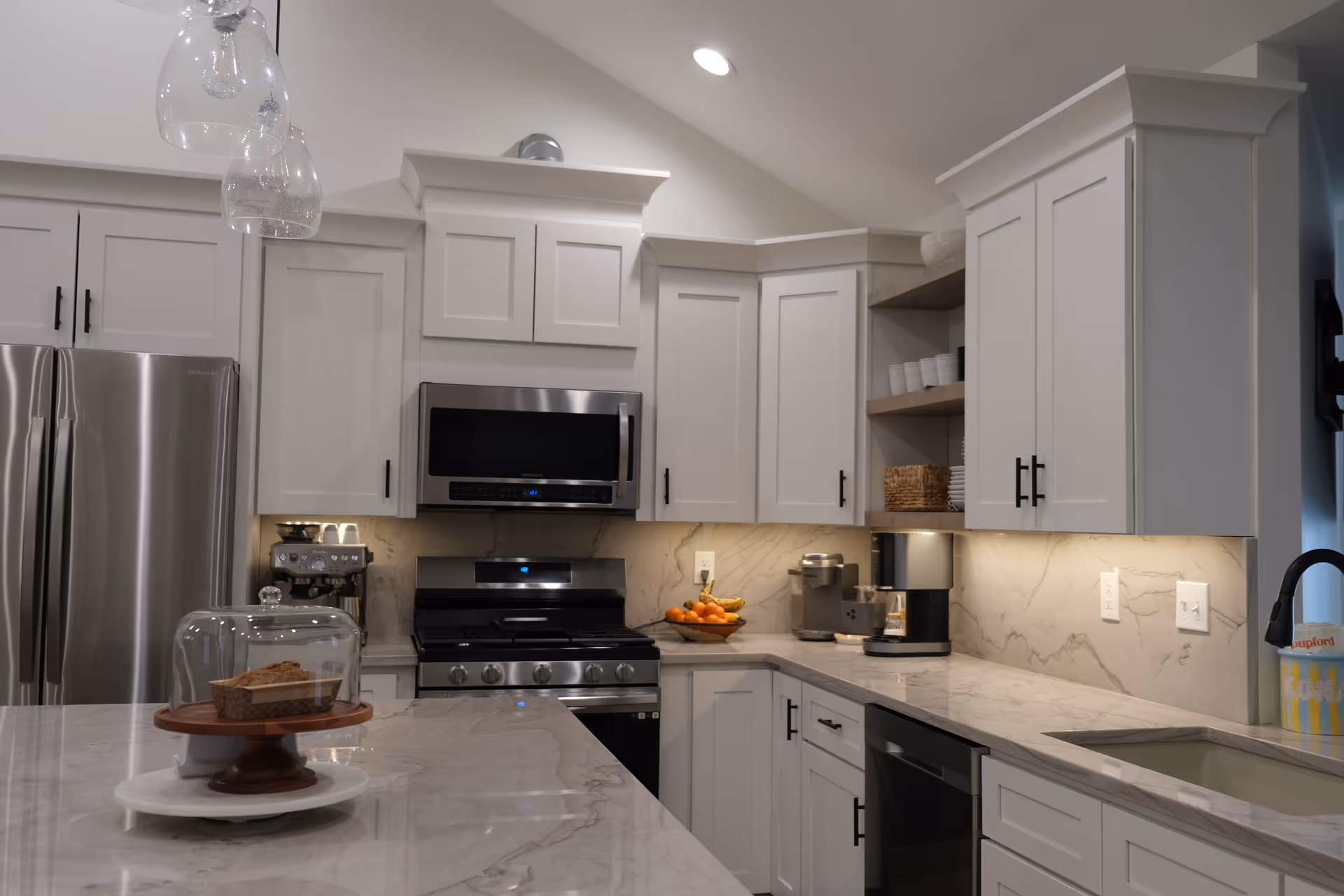 Modern white kitchen with marble countertops, stainless appliances, and an island.
