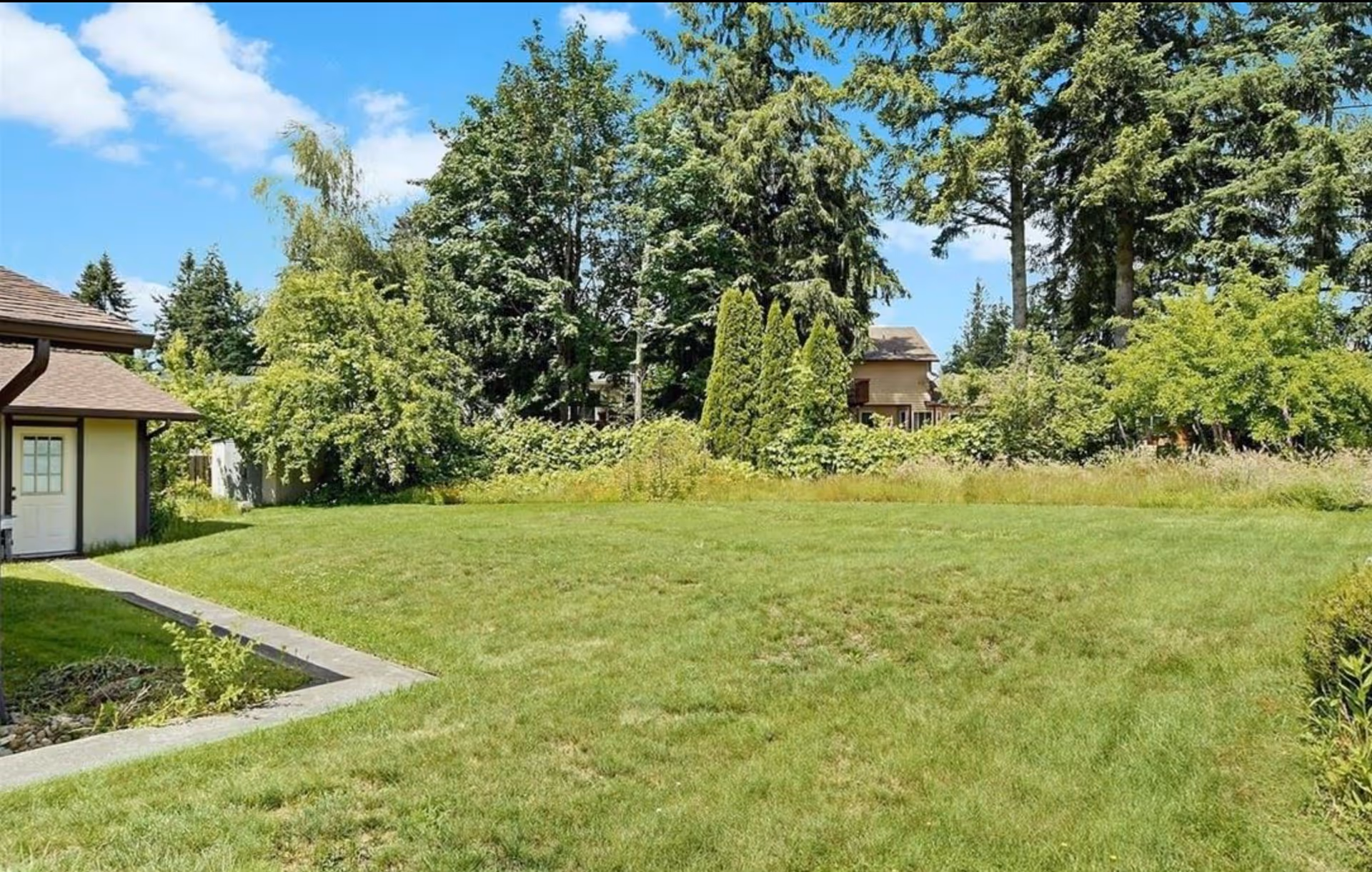 Exterior view of a grassy yard with trees and a building on the left.