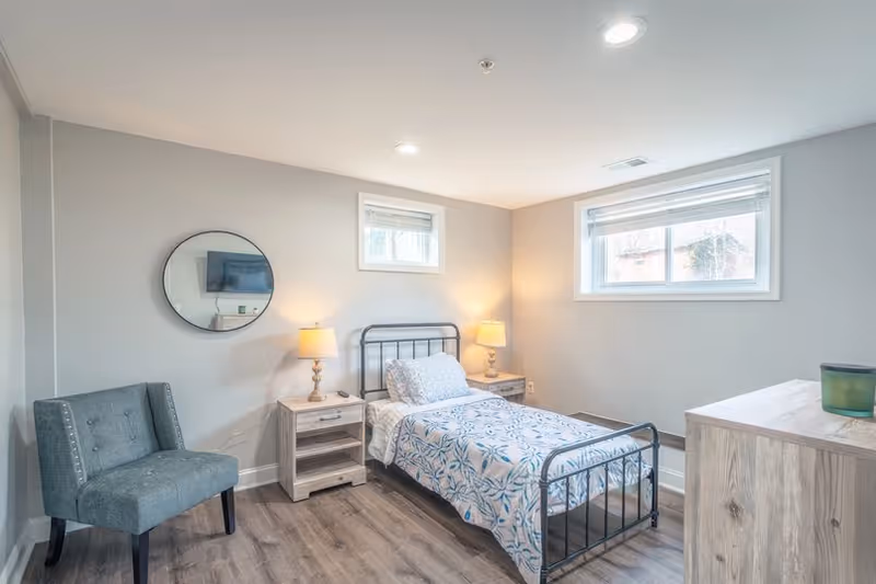 A cozy guest bedroom with a metal bed, nightstands, lamps, dresser, and gray walls.