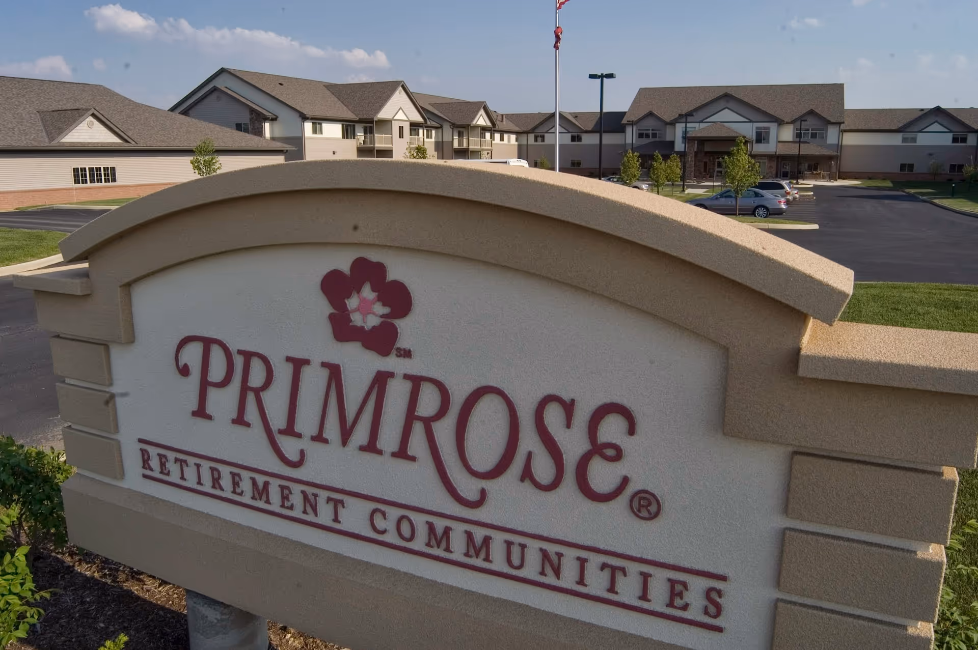 Front exterior view of Primrose Retirement Communities sign with campus buildings behind it.