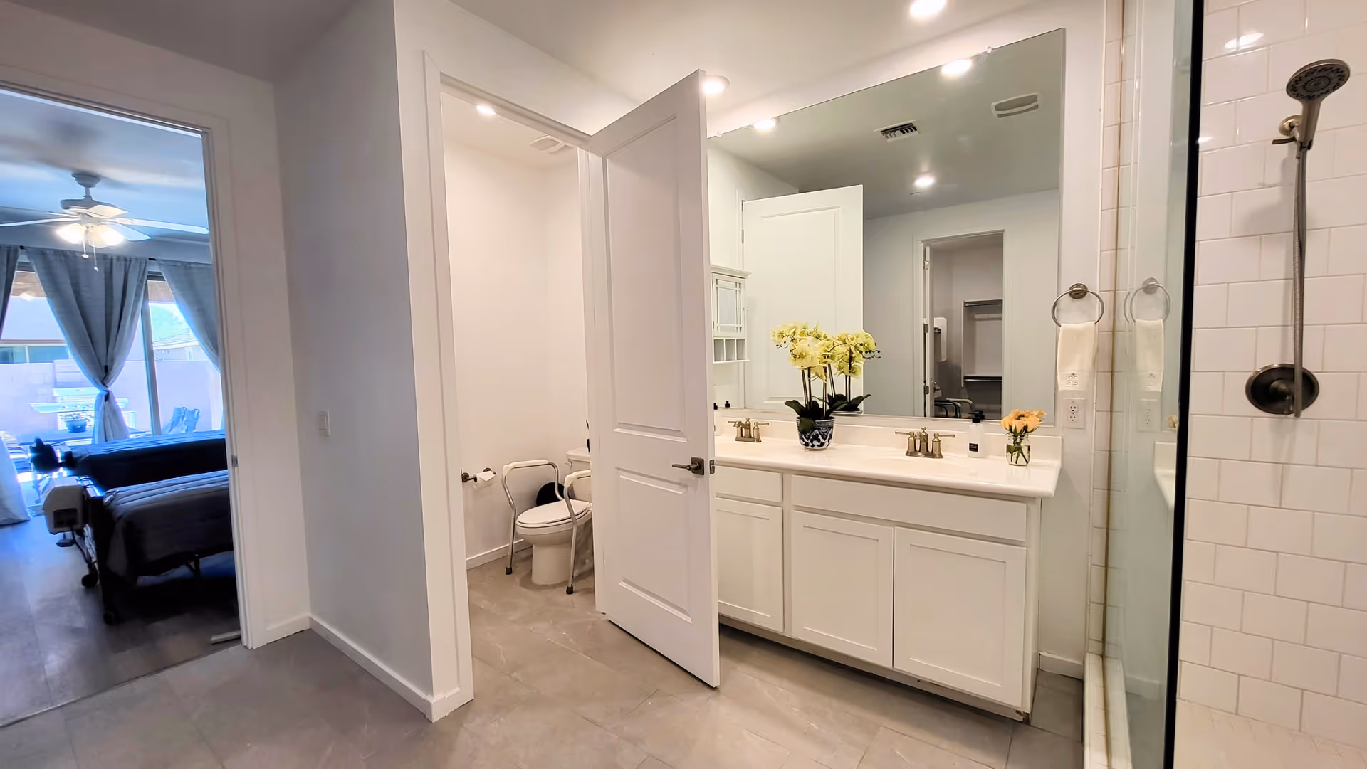Bright bathroom with double-sink vanity, glass shower, and doorway to bedroom.