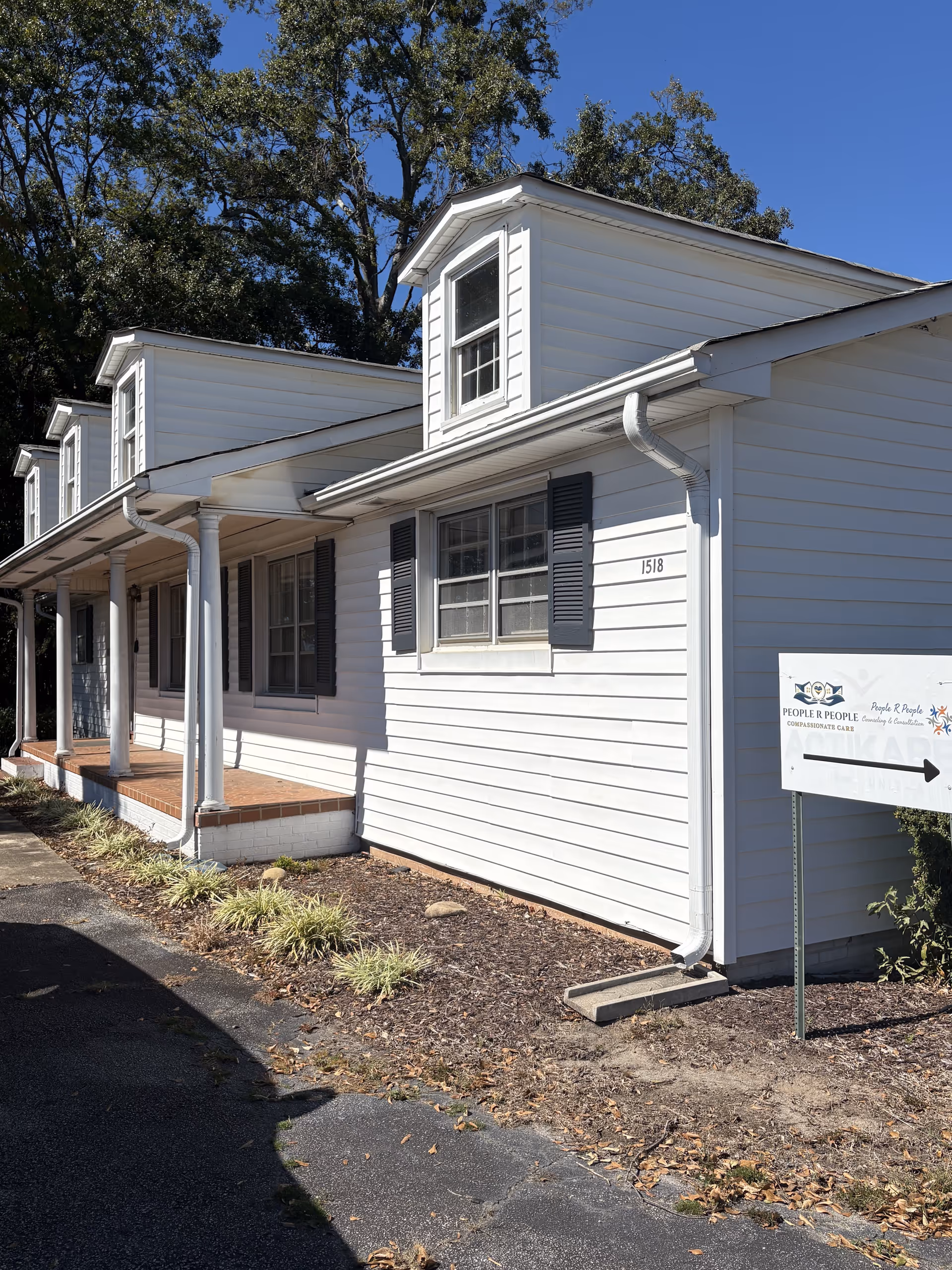 White, single-story facility exterior with a porch, windows, and a directional sign.