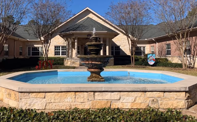 Stone fountain sits in a courtyard with a brick memory care facility in the background.