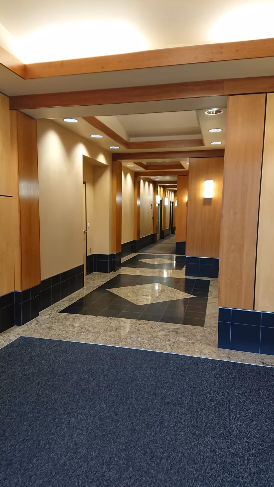 A well-lit beige hallway with wood-paneled walls and geometric tiled floor.