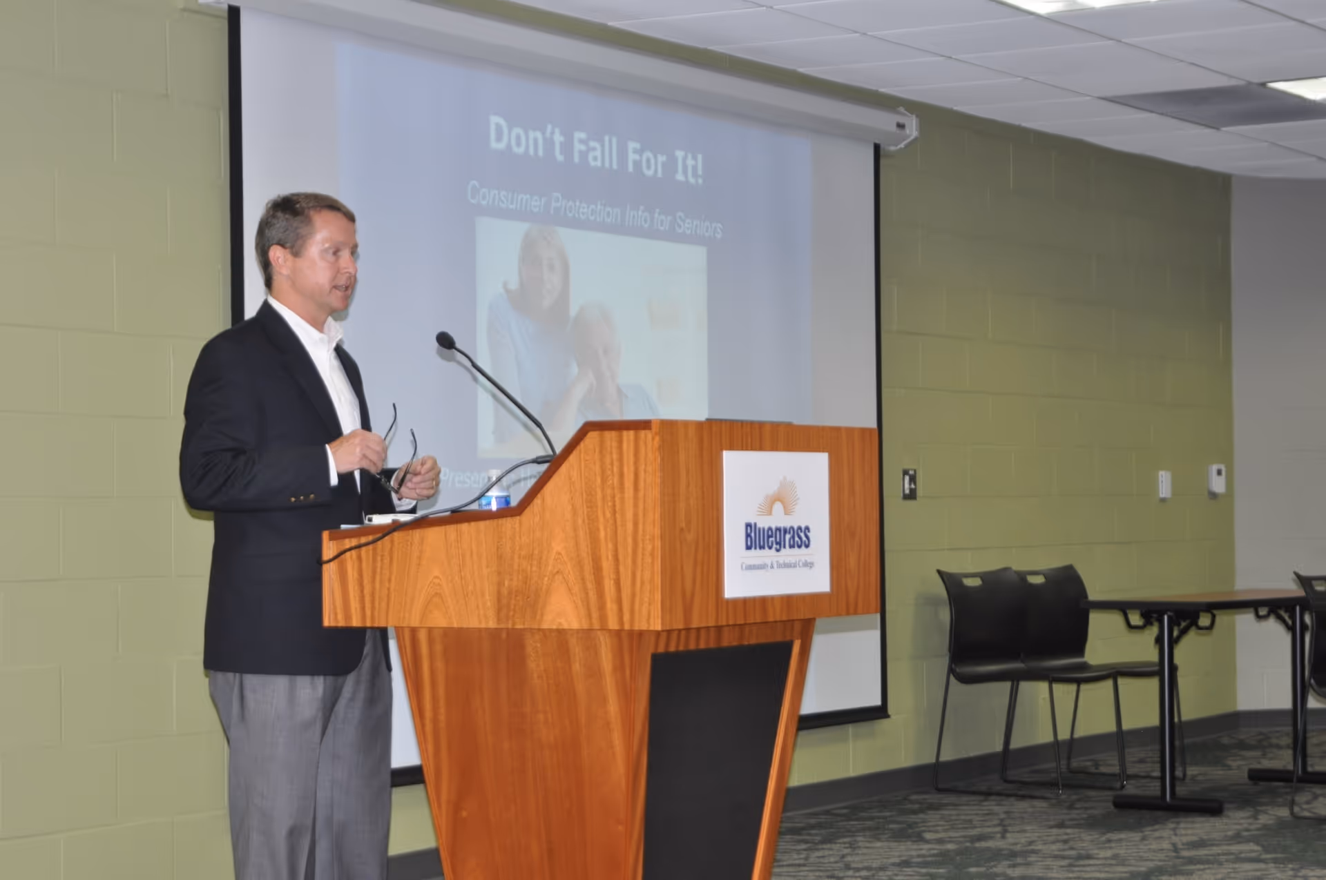 A man in a suit gives a presentation at a wooden podium in a conference room.