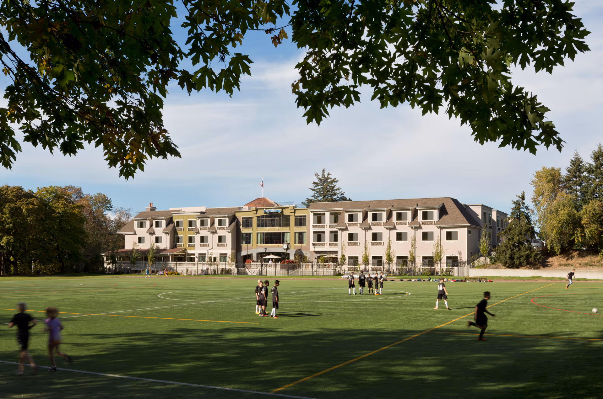 Aegis Living Queen Anne Rodgers Park exterior with a large sports field and players.