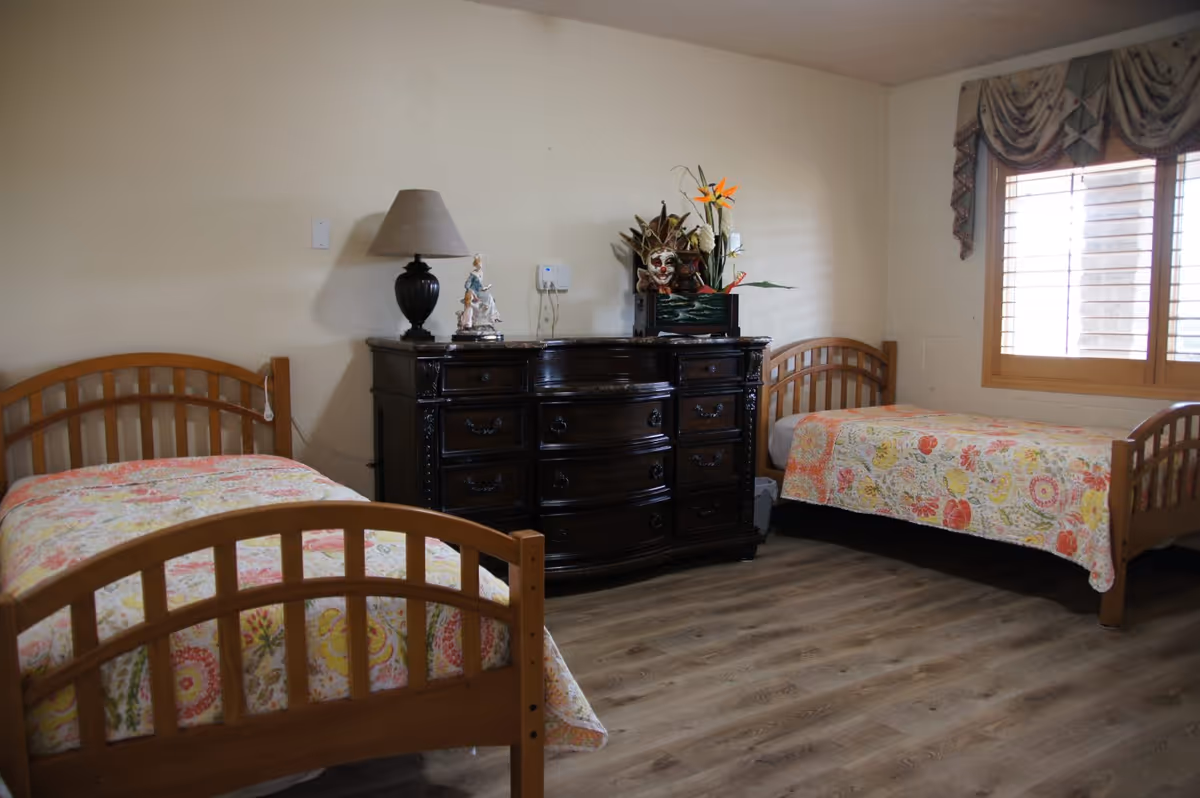 Two wooden beds with floral quilts flank a dark dresser in a bright bedroom.