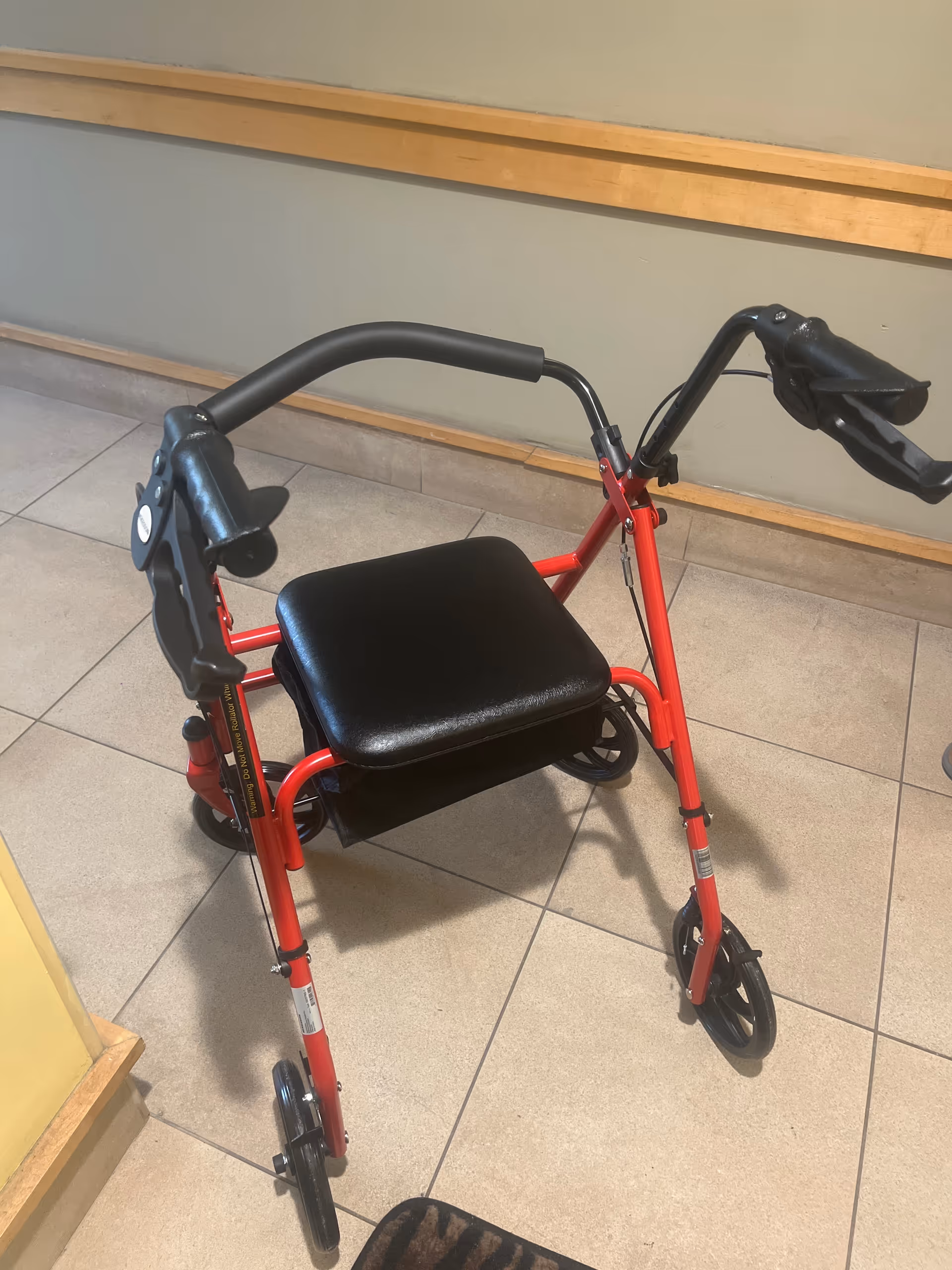 Red rollator walker with a black seat sits in a beige-tiled hallway