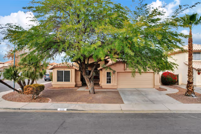Desert-style senior living facility front with pink stucco, large trees, and a two-car garage.