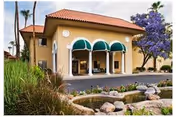 Front exterior of a tan stucco senior living building with green arched awnings.