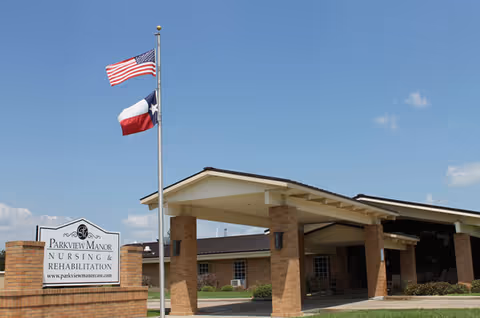Exterior view of Parkview Manor Nursing and Rehabilitation with entrance canopy and flags.