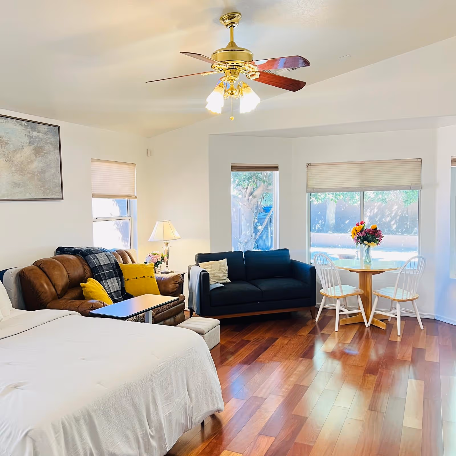 Bright living area featuring a brown sofa, bed, round dining table, and large windows.
