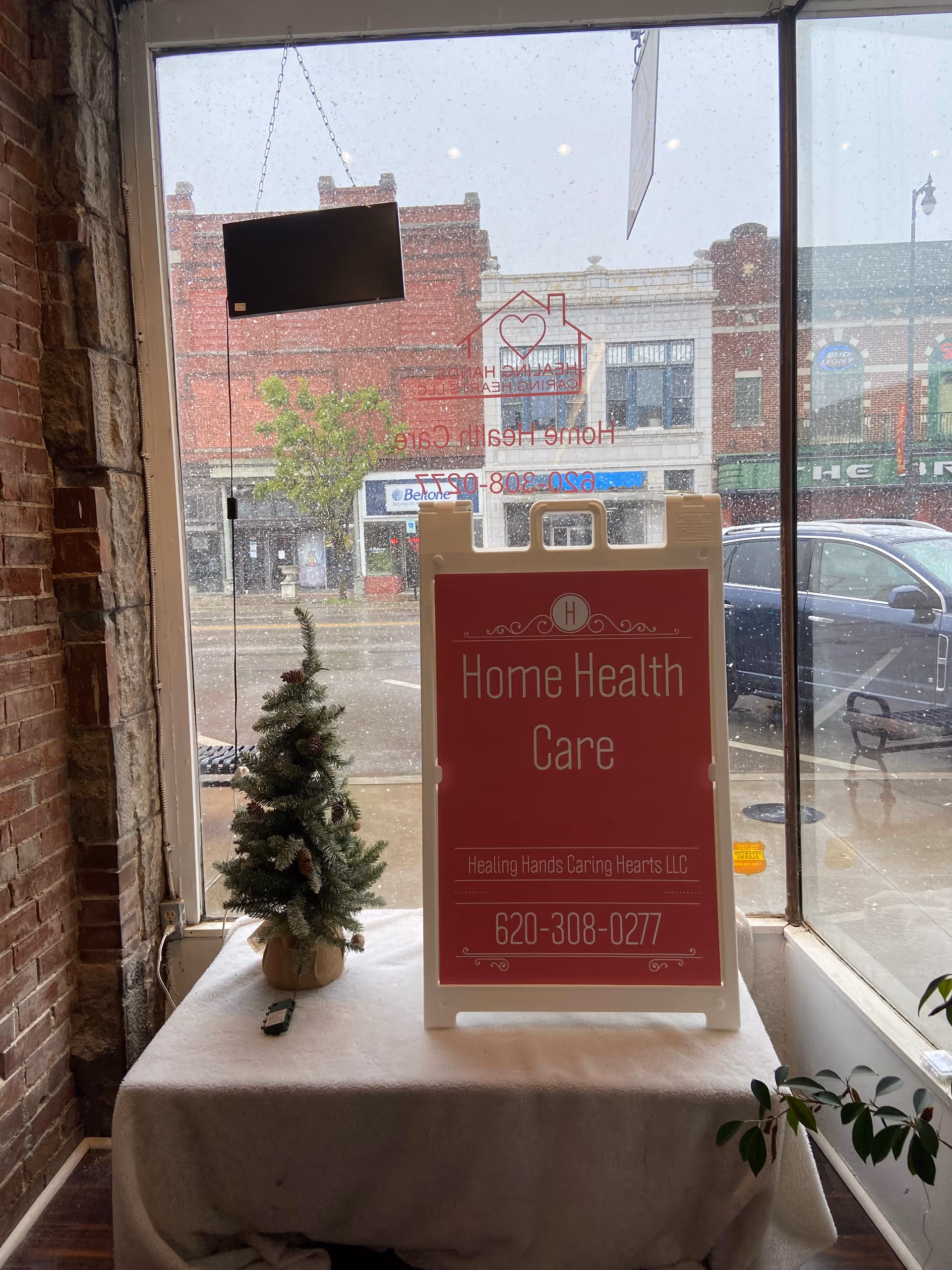Small Christmas tree and a red Home Health Care sign on a table by a window