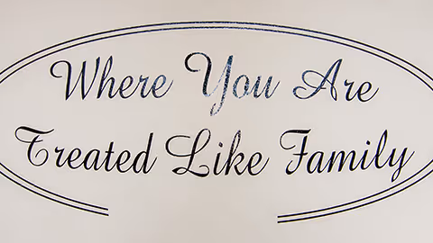 A decorative wall sign with the phrase 'Where You Are Treated Like Family' written in elegant cursive font inside an oval border.