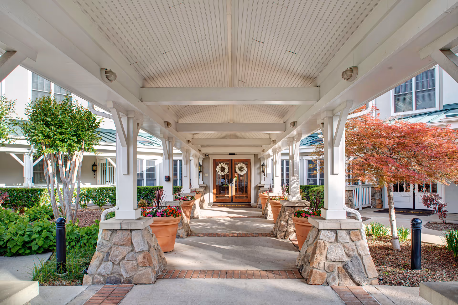 Covered walkway leads to double wooden doors at Sunrise on Hillcrest, flanked by planters.