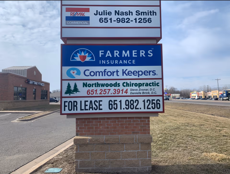 Tall outdoor sign panel advertising Comfort Keepers and other businesses beside a road.