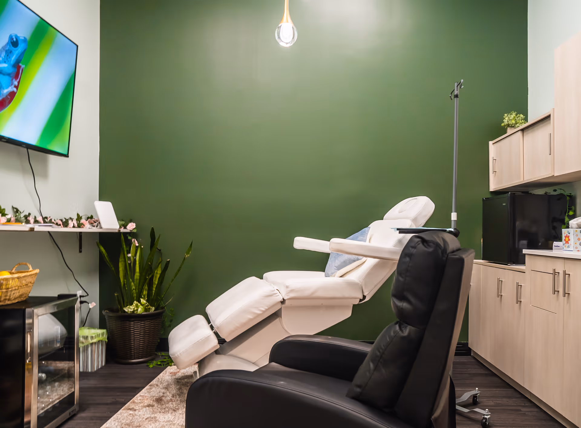 White reclining chair in a modern treatment room with green wall and cabinets.