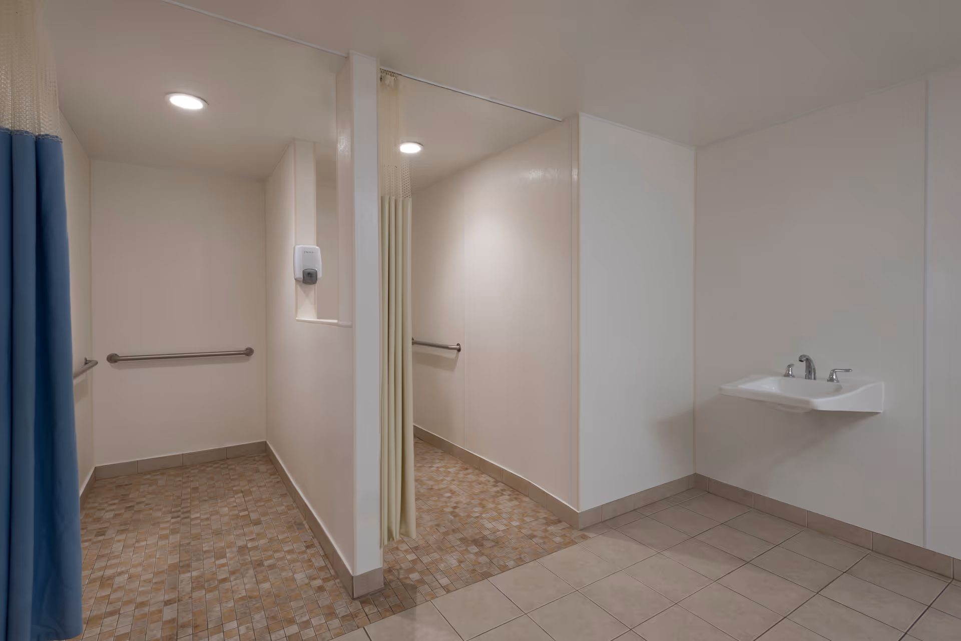 Public bathroom with shower stalls, blue curtain, and wall-mounted sink in a senior facility.