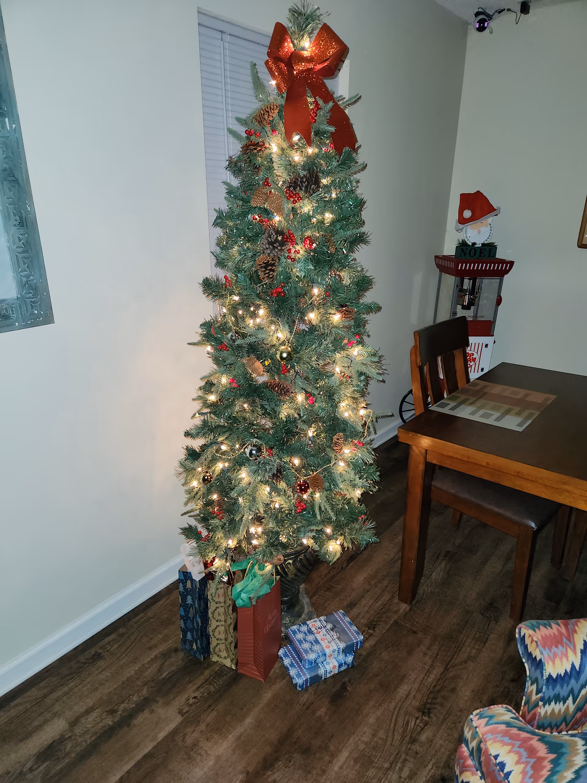 Decorated Christmas tree with wrapped gifts beside a dining table in a cozy corner.