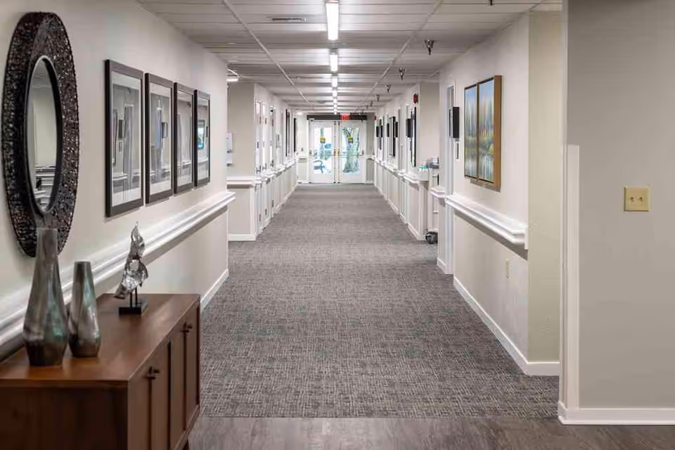 A long, well lit hallway in a senior living facility with framed artwork.