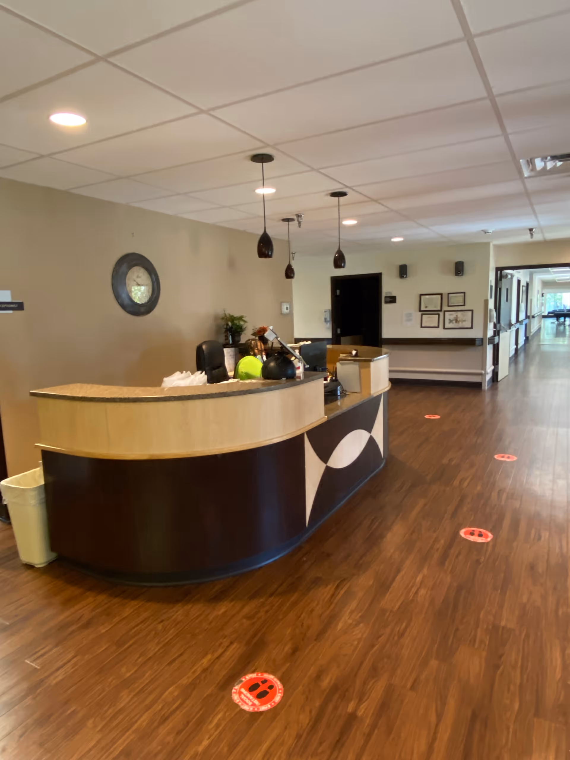 A reception/nursing station in a senior care facility hallway with pendant lights, wood floors, and social distancing floor markers.