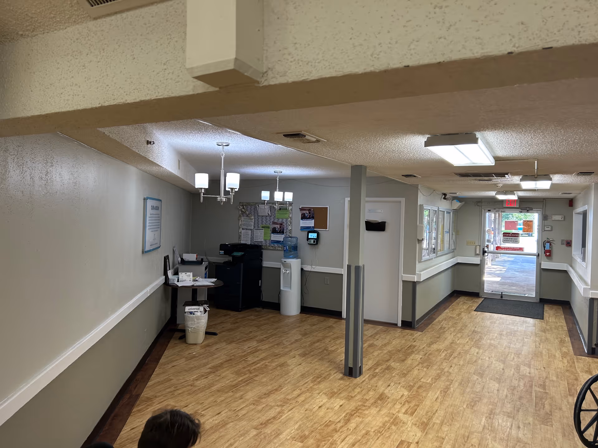 Interior hallway of a senior living facility with a reception desk, bulletin boards, and glass entrance.