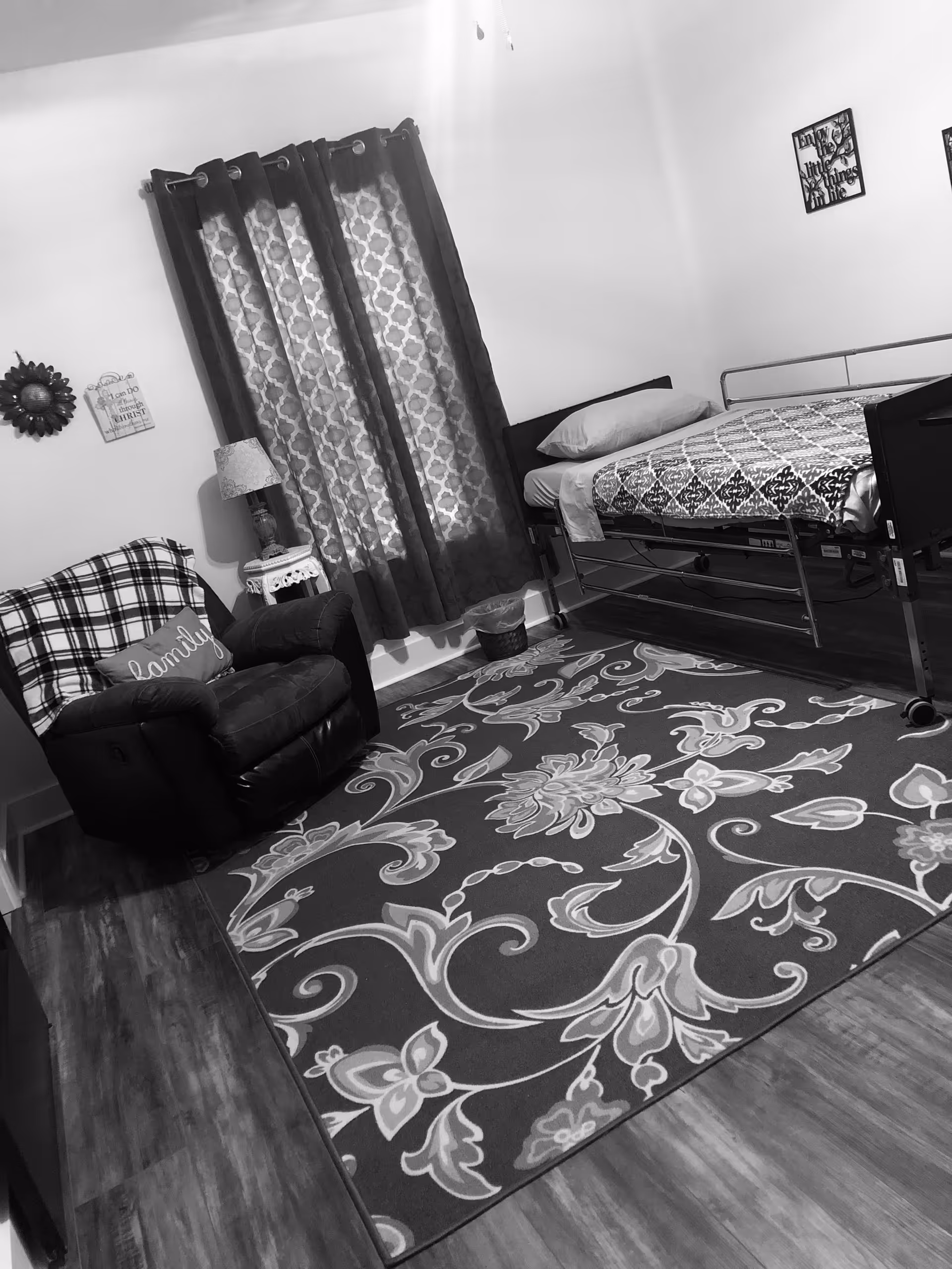 A bedroom in a senior living facility with a bed, chair, and patterned rug.