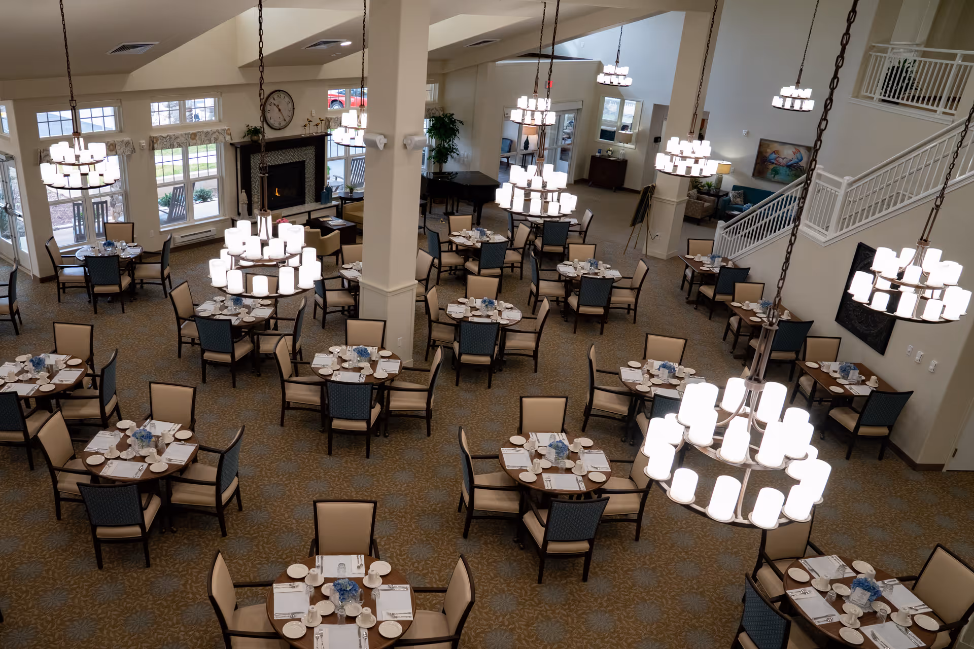 Large, well-lit dining room with multiple round tables set for meals and hanging chandeliers.