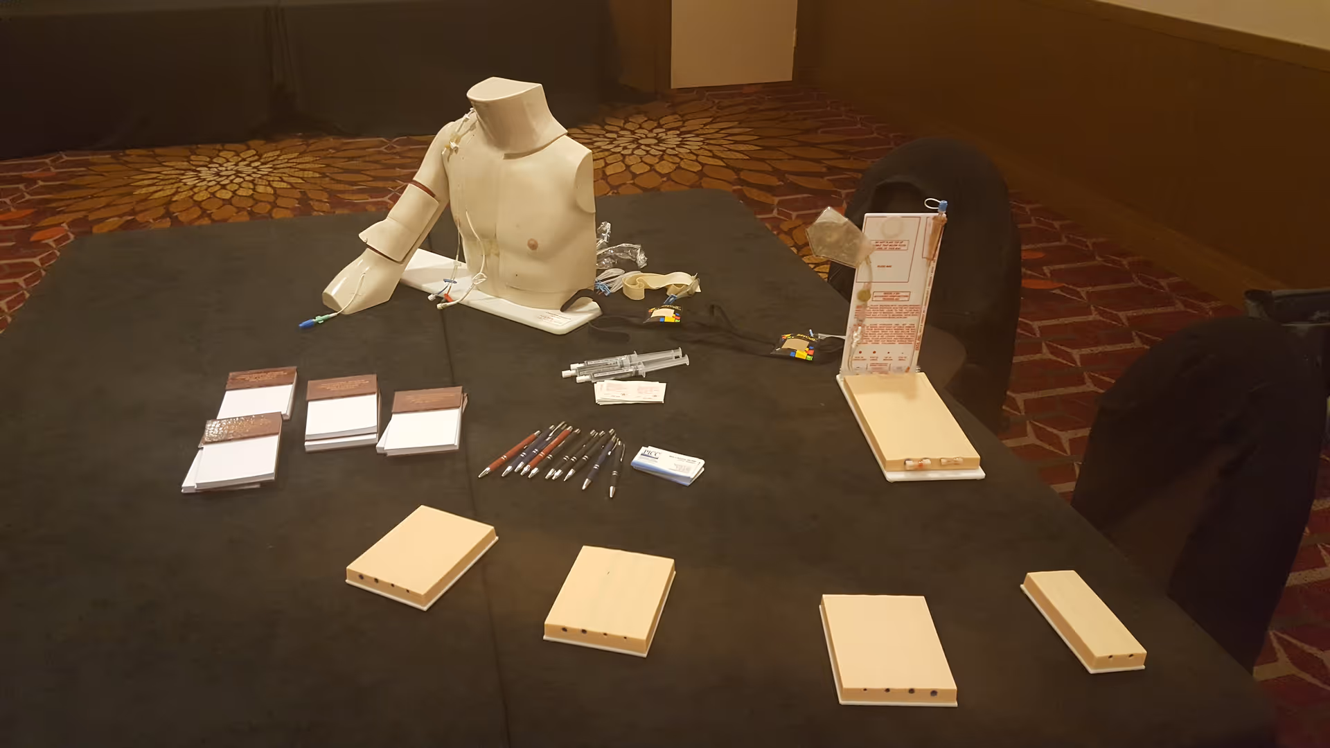 Table setup with a mannequin torso and assorted parts, pens, and brochures.