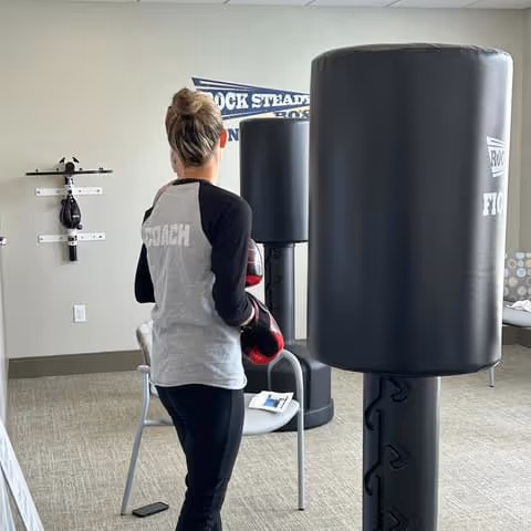 A person in athletic wear punches a tall black bag in an indoor fitness room.