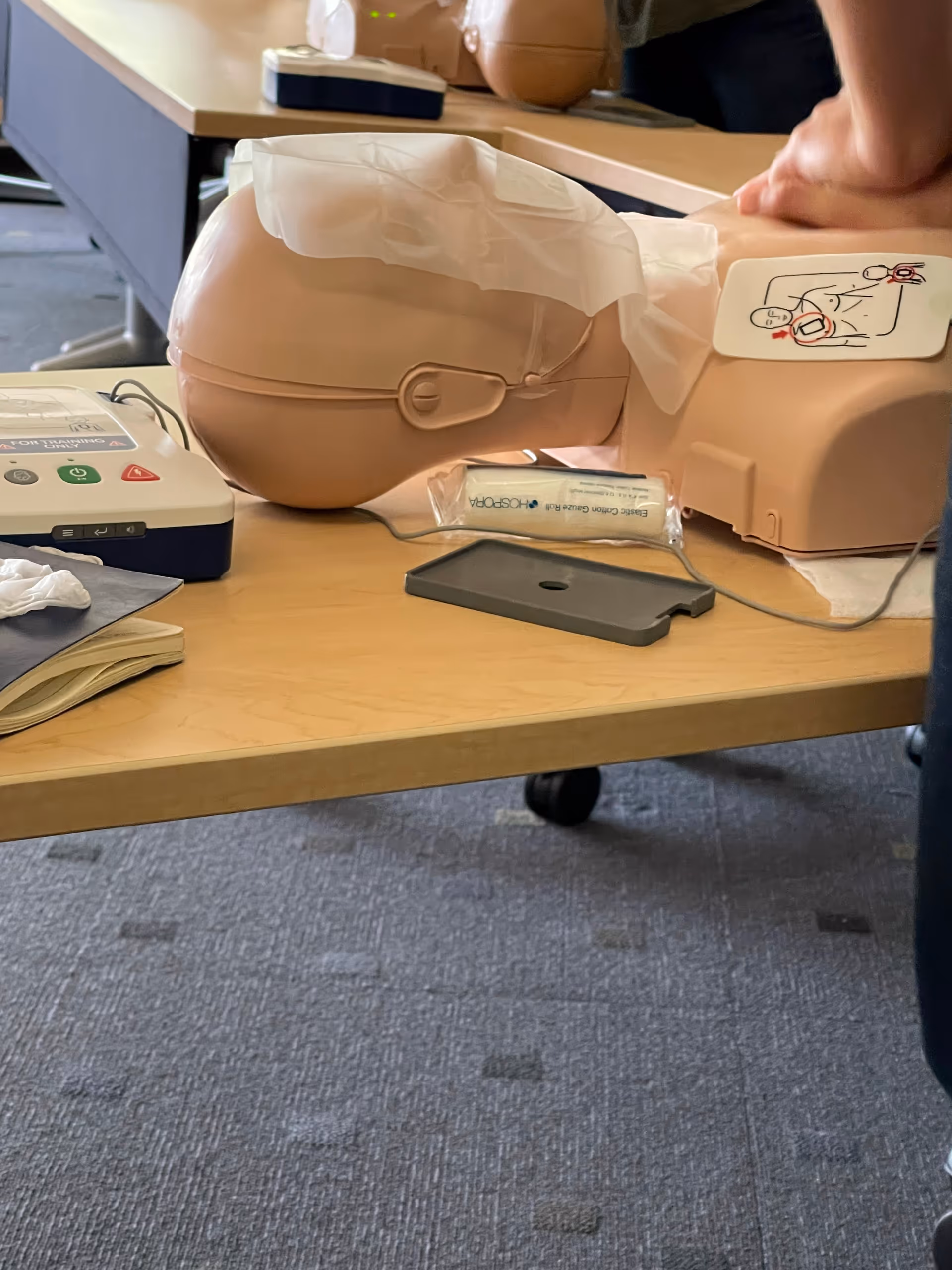 A medical training mannequin with AED equipment on a table.
