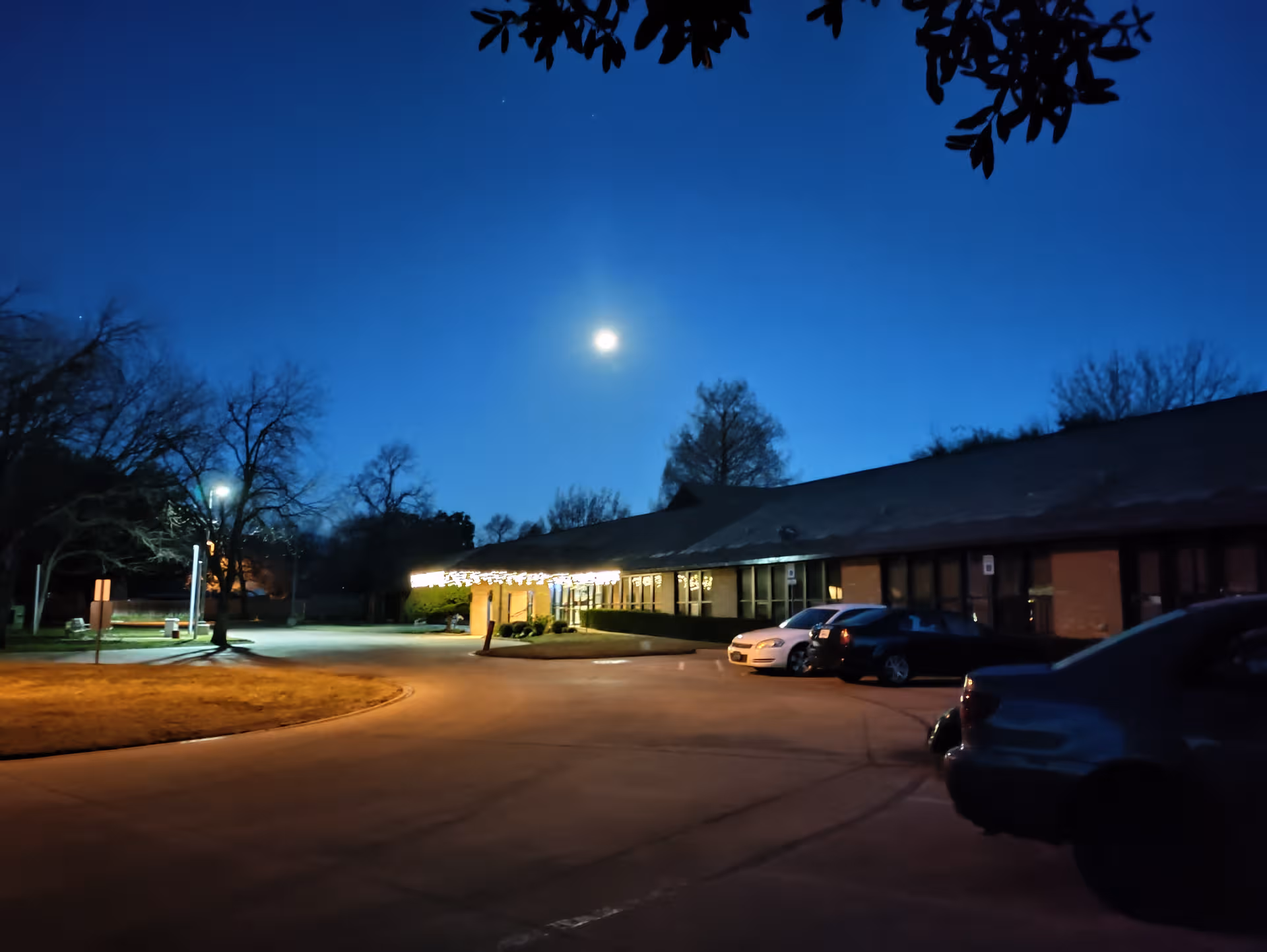 Night exterior of Meadow View Assisted Living with glowing entrance and parked cars.