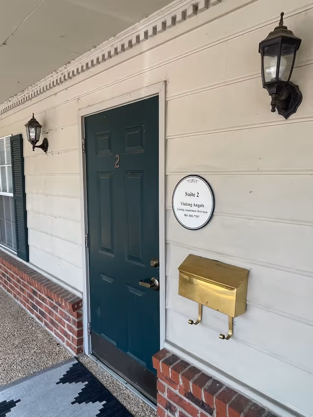 Exterior view of a building entrance with a door, plaque, and gold mailbox.