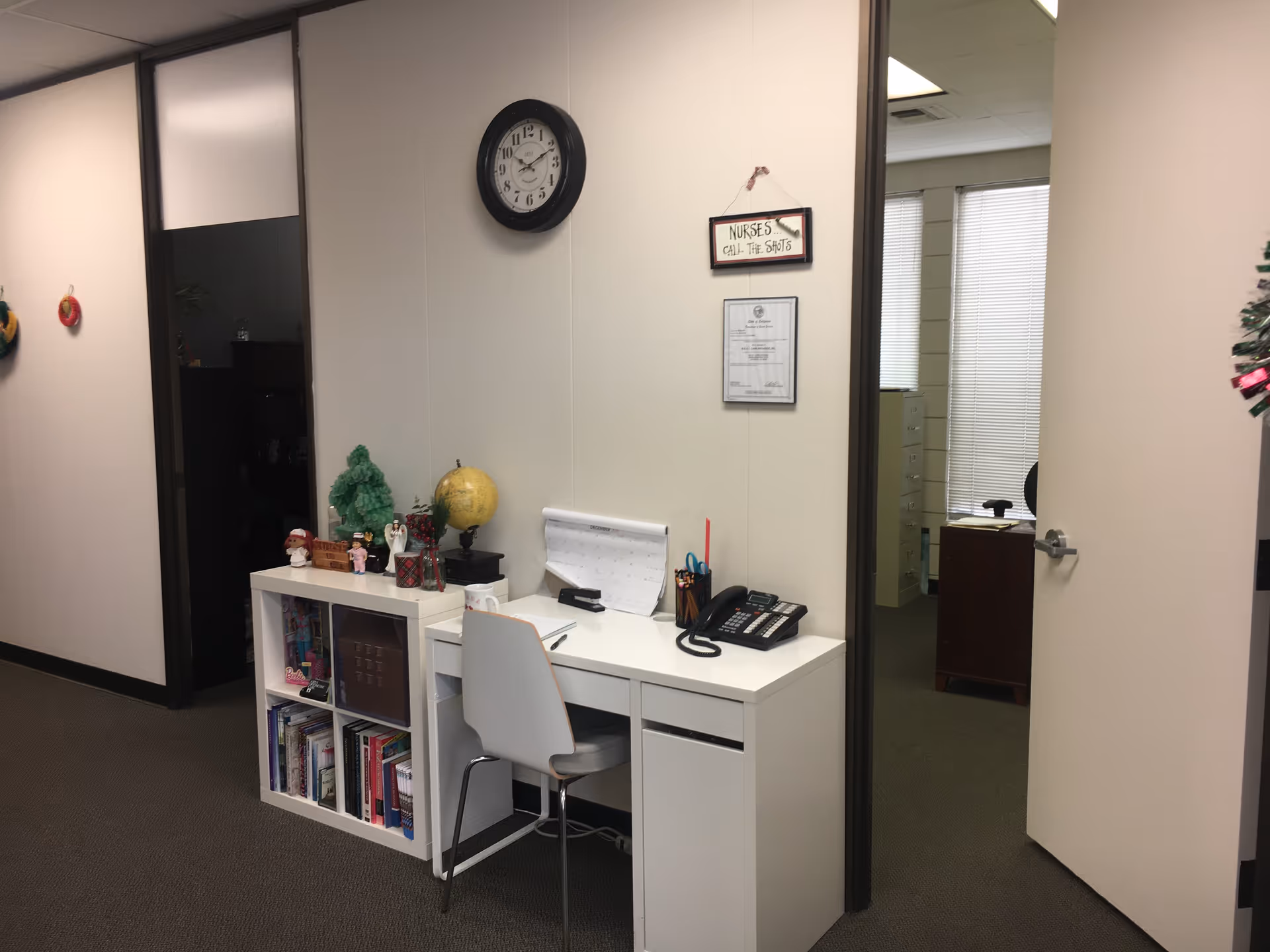 White desk with chair and office items in a small administrative area, clock on wall.