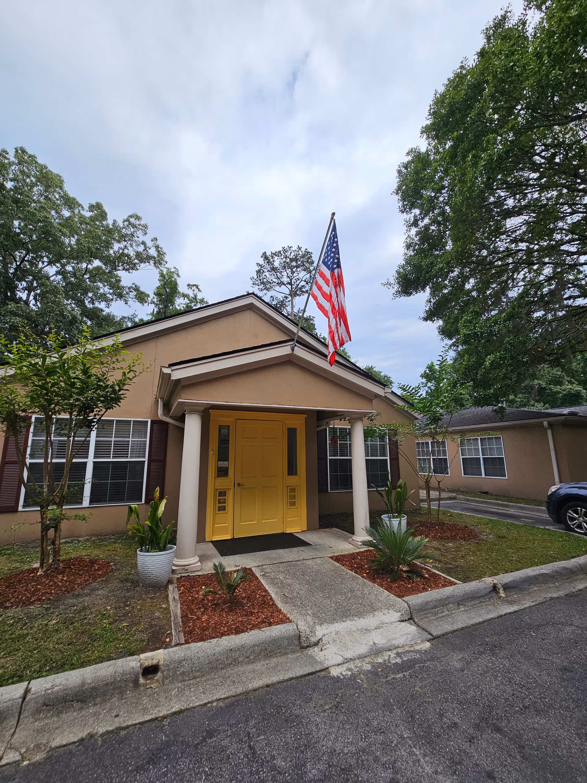 Front entrance of a senior living facility with a yellow door and American flag