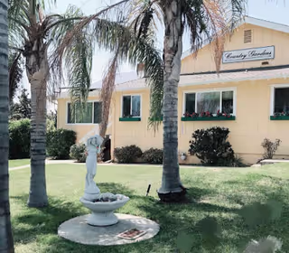 Yellow Country Gardens facility front with palm trees, a fountain, and green shutters.