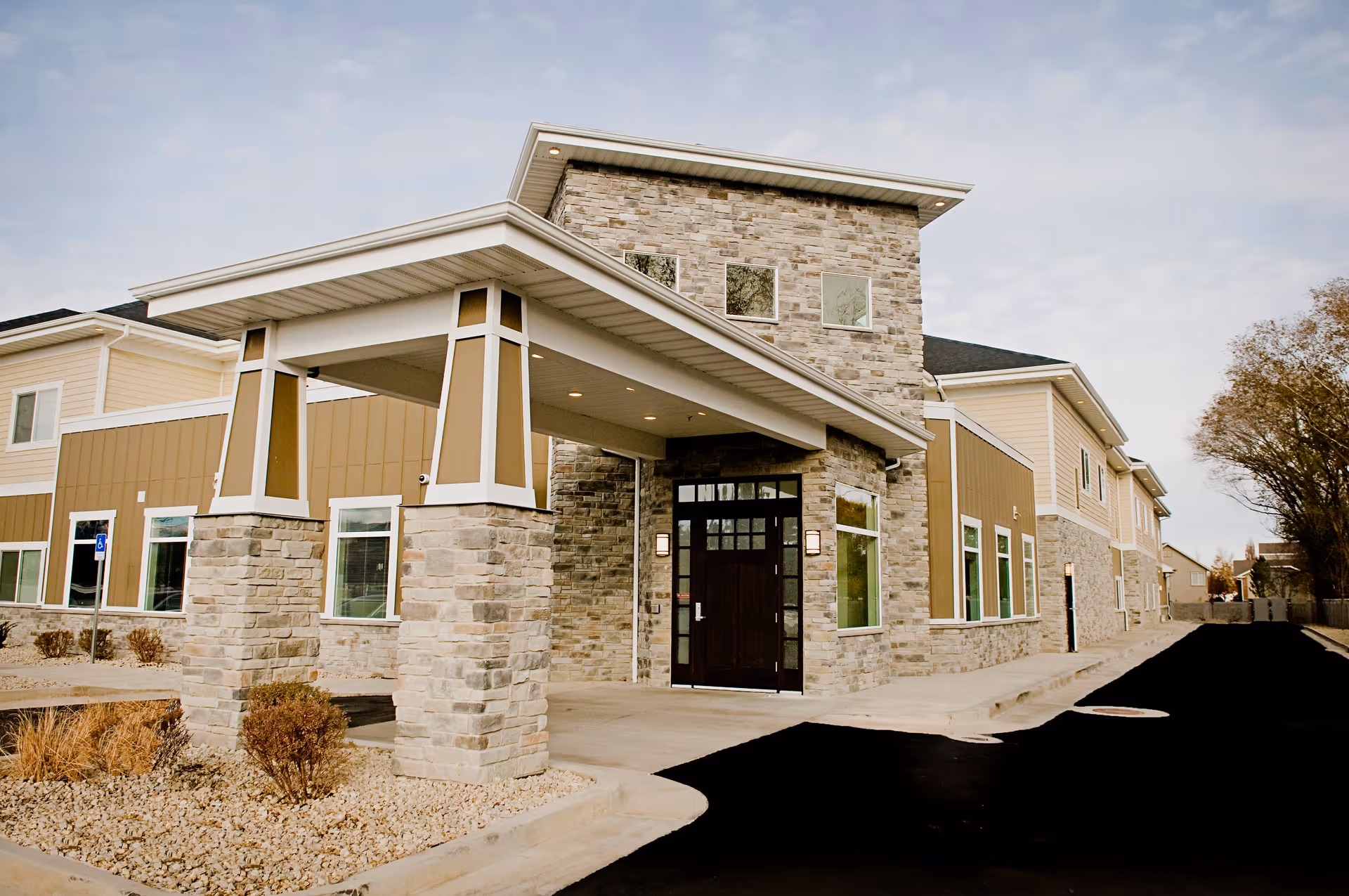Riverway Assisted Living exterior featuring stone columns, covered entrance, and landscaped surroundings.