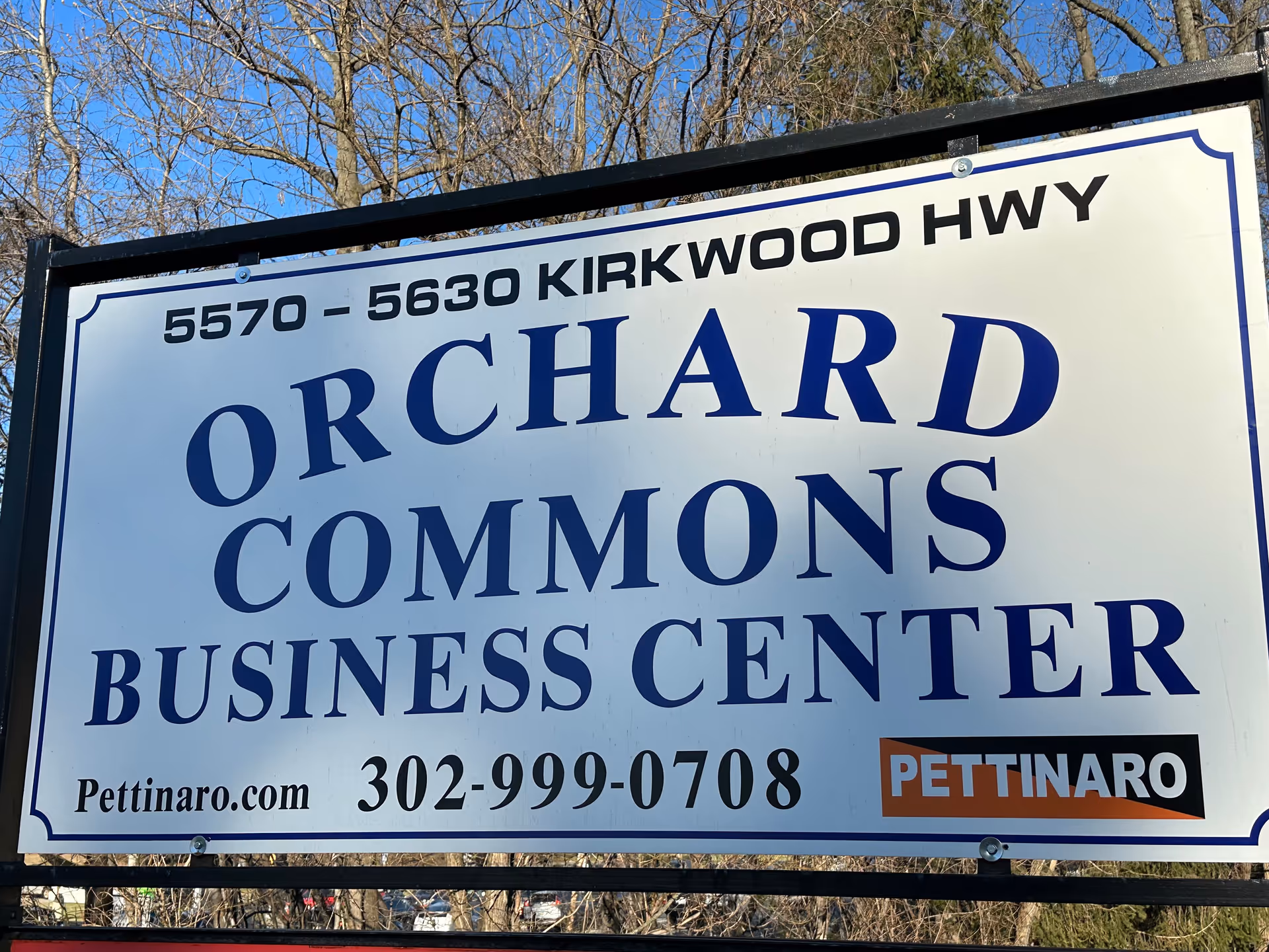 Outdoor sign reading Orchard Commons Business Center with blue lettering