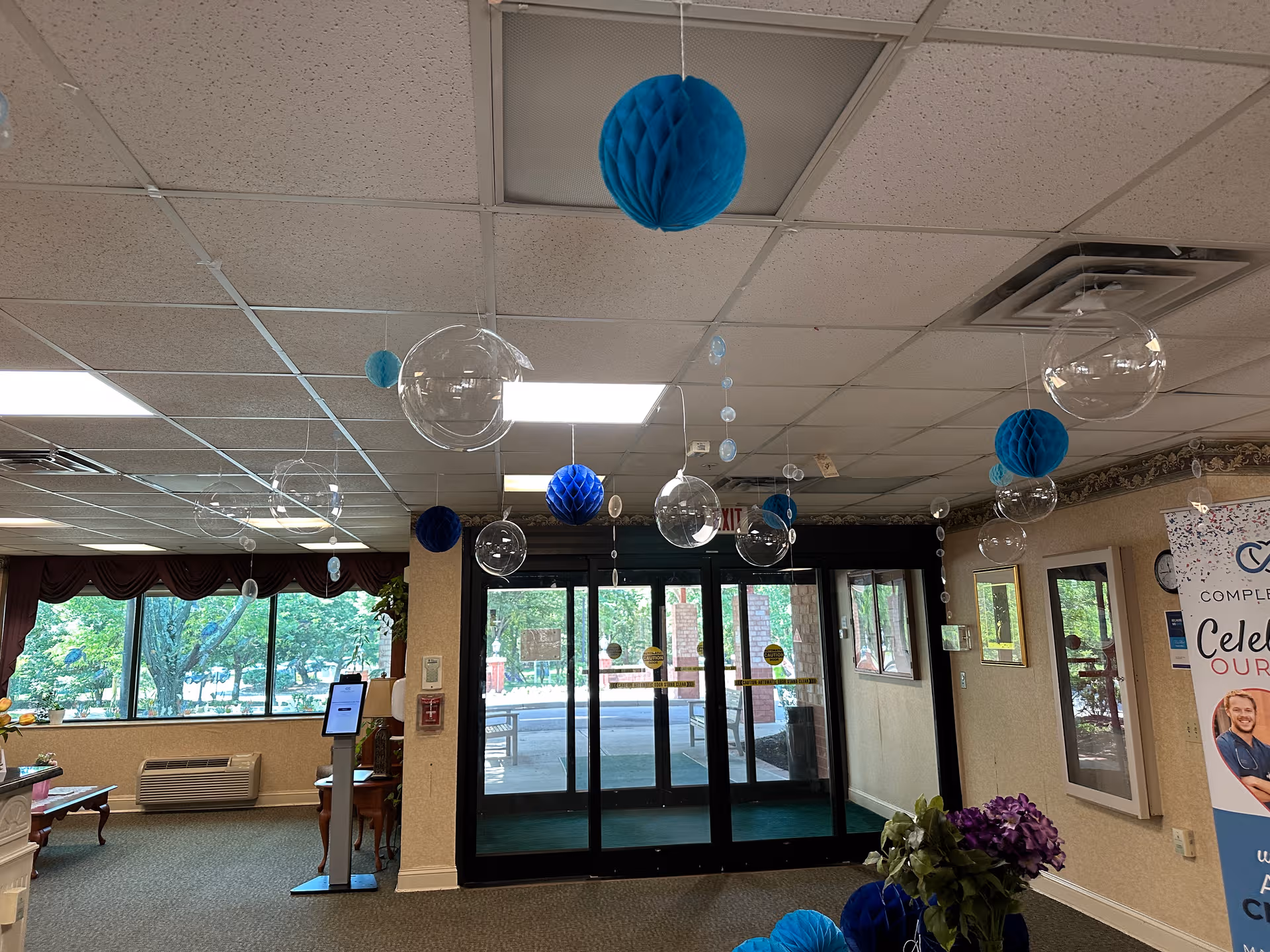 Lobby area with blue hanging decorations and glass entrance doors inside a senior living facility.