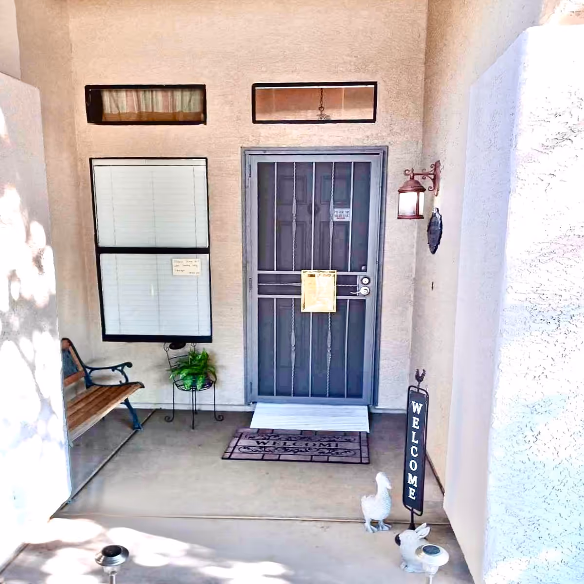 Front porch entry with metal door, bench seating, and welcome signs.