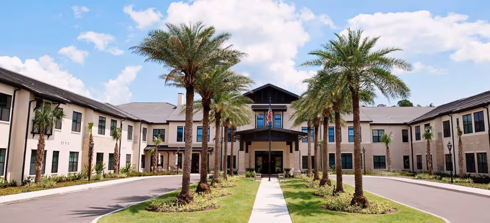Exterior view of Starling at Nocatee Assisted Living facility with palm trees and a central entrance.