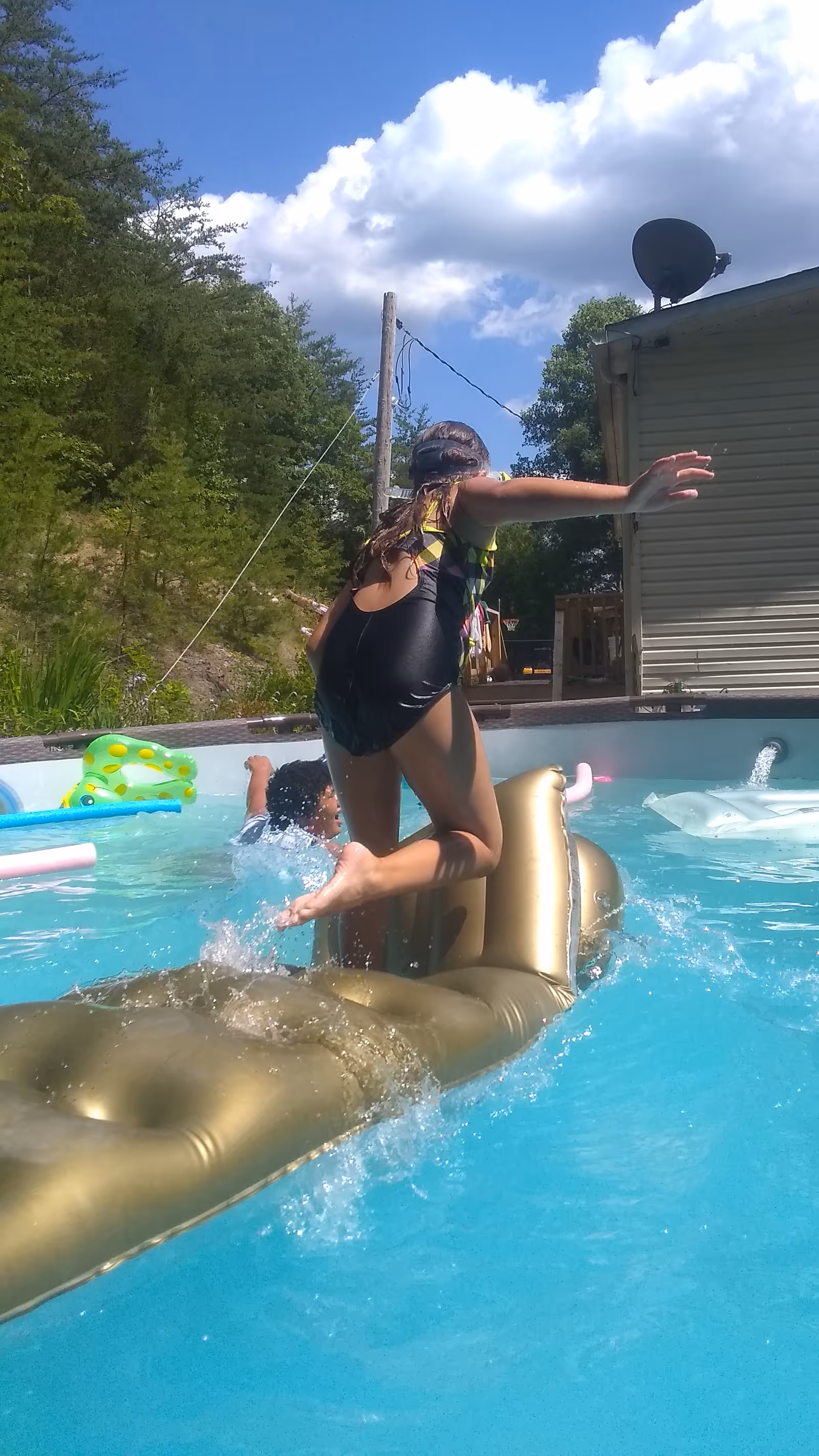 A person in a black swimsuit leaps onto an inflatable in an outdoor pool.