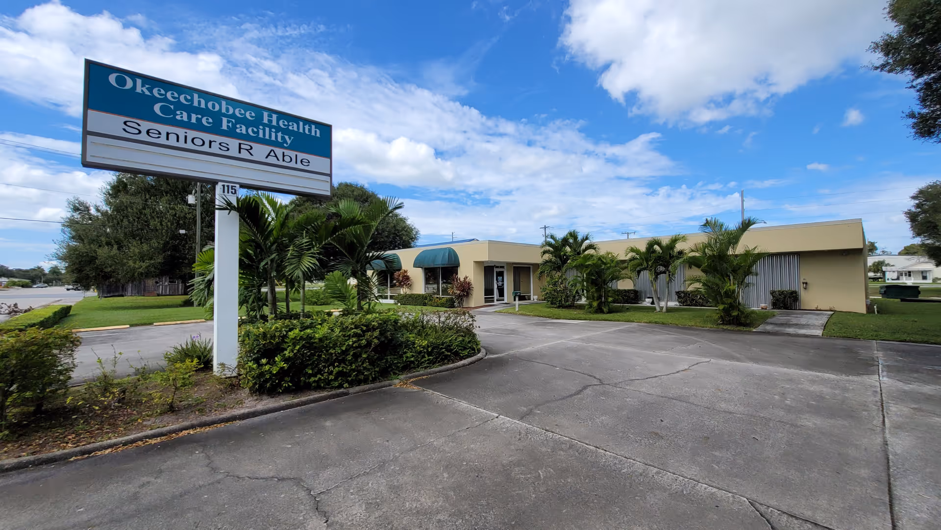 Exterior view of a senior care facility with a large sign and tropical landscaping.