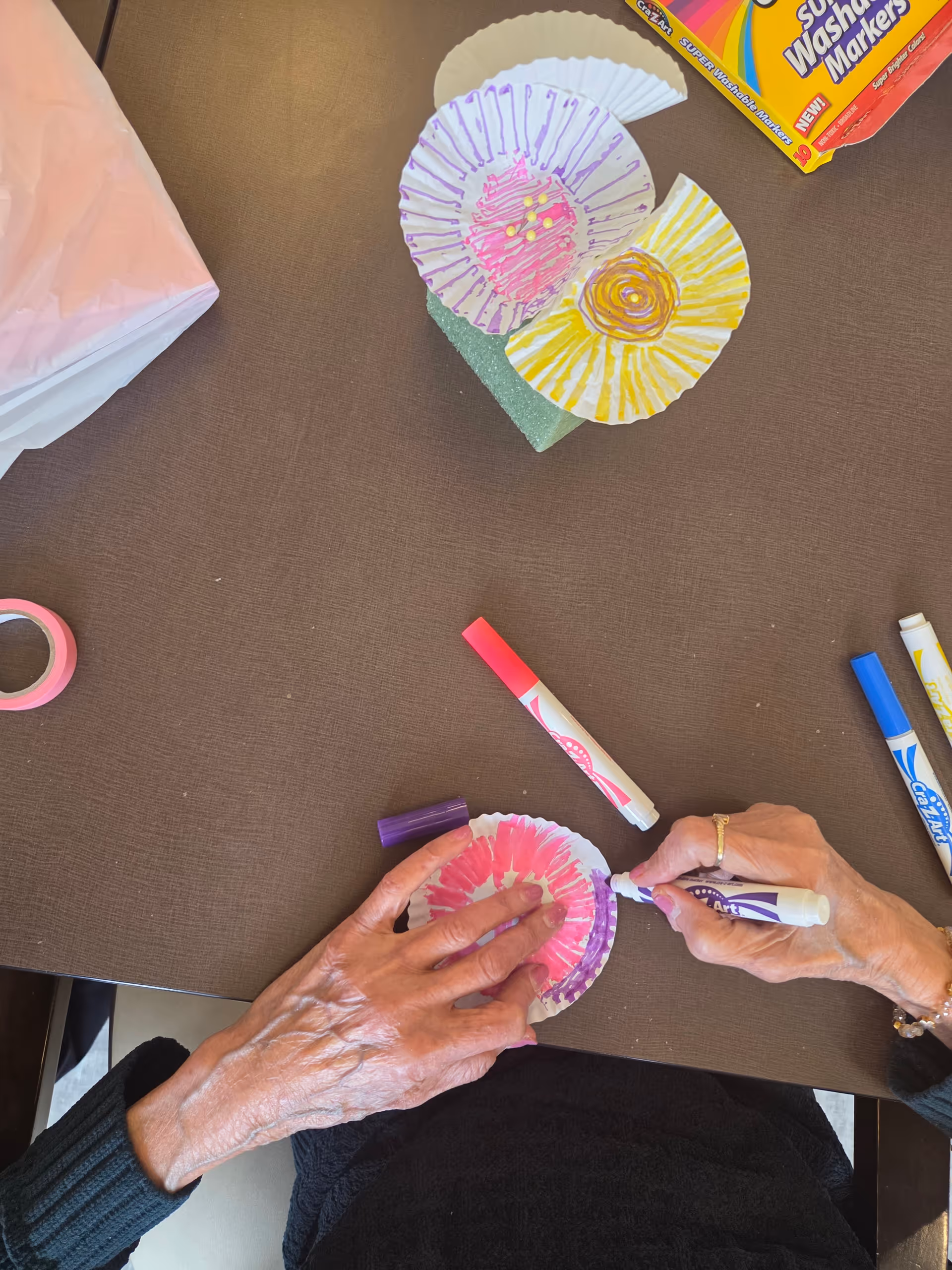 Elderly hands craft paper decorations at a table with markers